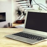 Sleek laptop on a wooden desk with blurred contemporary home interior in the background.